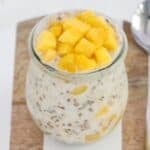 Creamy mango overnight oats in a glass jar on a wood and white serving tray.