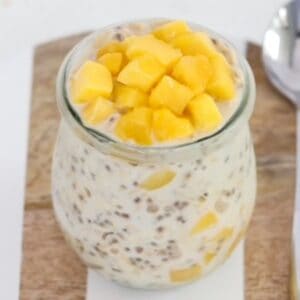Creamy mango overnight oats in a glass jar on a wood and white serving tray.