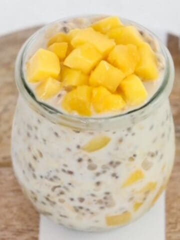 Creamy mango overnight oats in a glass jar on a wood and white serving tray.