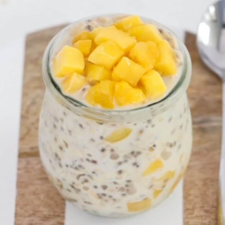 Creamy mango overnight oats in a glass jar on a wood and white serving tray.