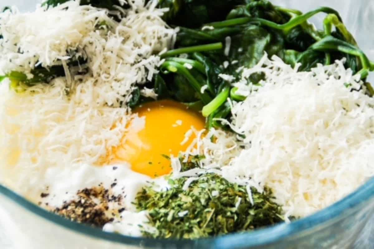 Cottage cheese, egg, parmesan cheese, salt, pepper, and spinach, unmixed, in glass bowl.