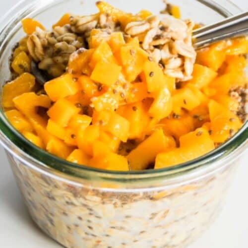 Mango overnight oats with a spoon in a glass jar.