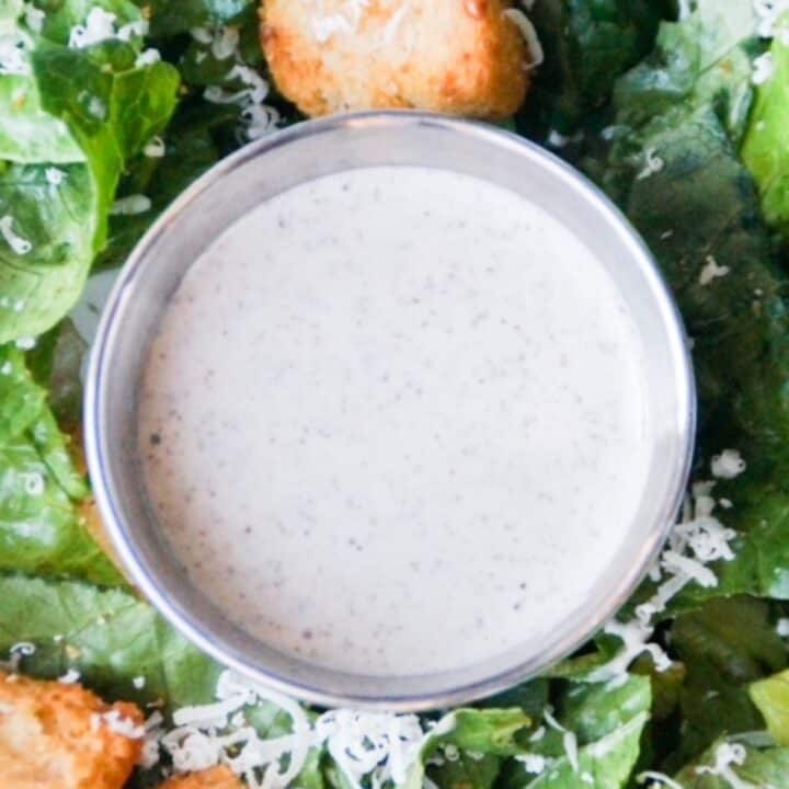 Caesar dressing in a small round container centered around salad