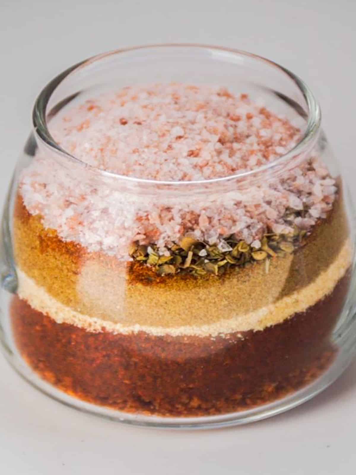 Six spices and pink sea salt layered in a small glass jar.