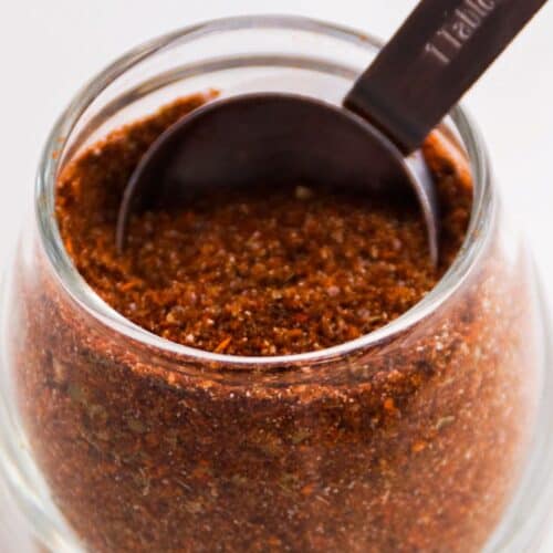 Taco seasoning in a glass jar with a measuring spoon.
