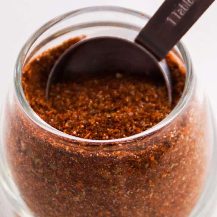 Taco seasoning in a glass jar with a measuring spoon.