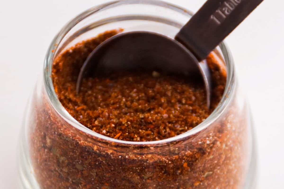 Taco Seasoning in a glass container with a measuring spoon