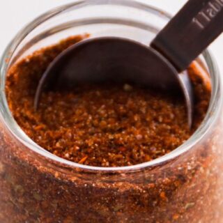 Up close image of taco seasoning in a small glass container being scooped up using a tablespoon.
