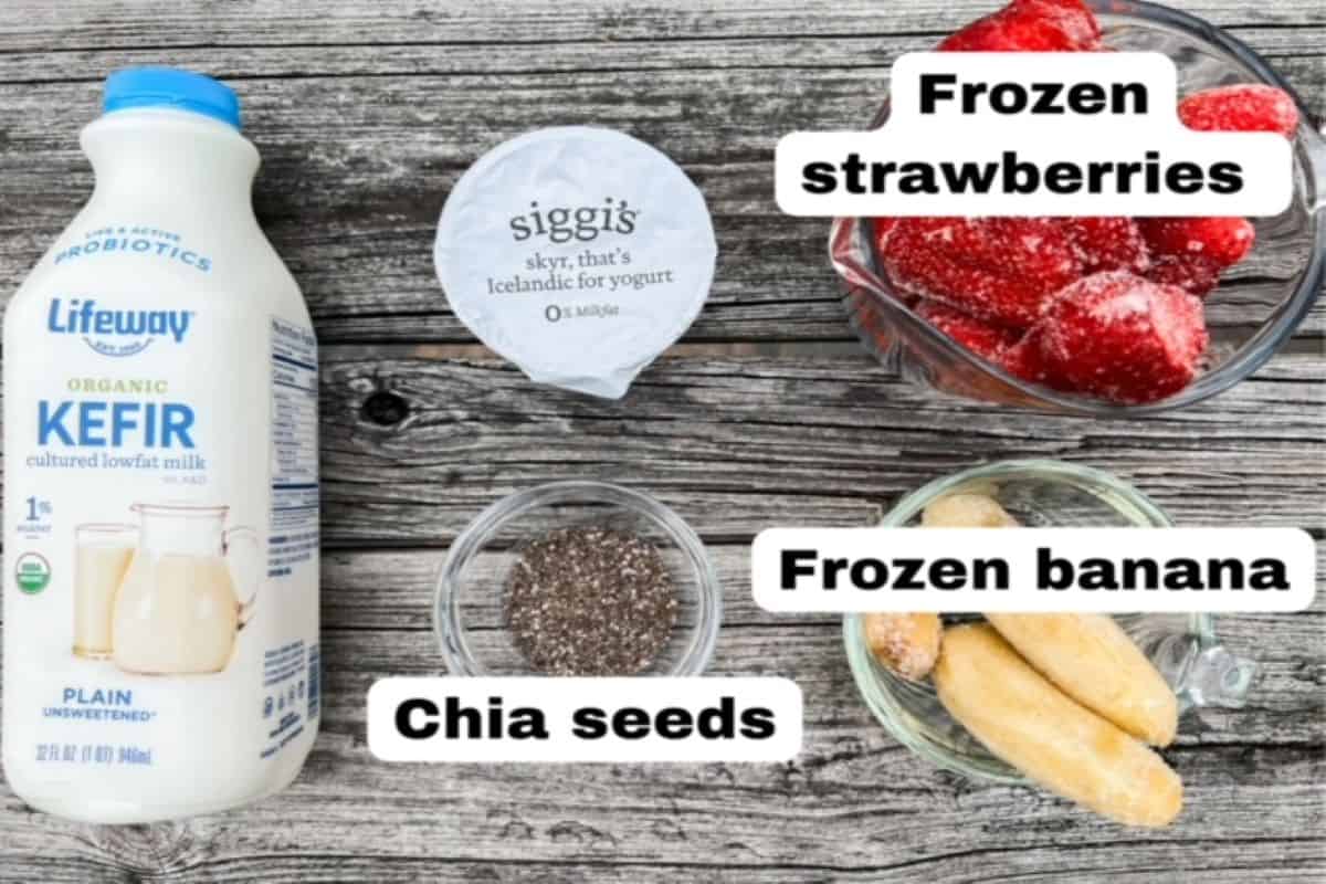 One bottle of plain kefir, one container of Skyr, chia seeds labeled, strawberries in a bowl, labeled, and frozen banana pieces in a bowl, labeled.