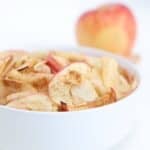 Air fried apple slices in a white bowl with an apple in the background.