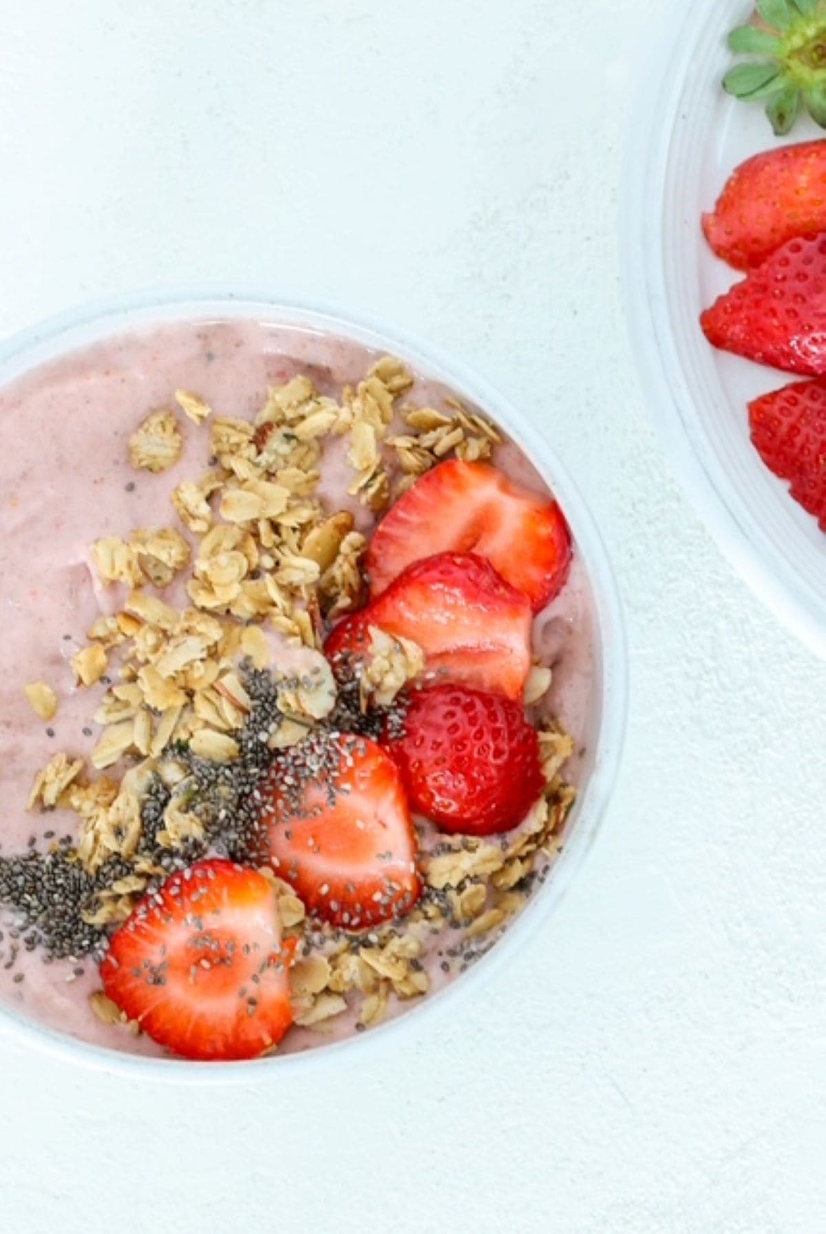One Strawberry Smoothie Bowl in a white bowl, topped with granola, sliced strawberries, and chia seeds.