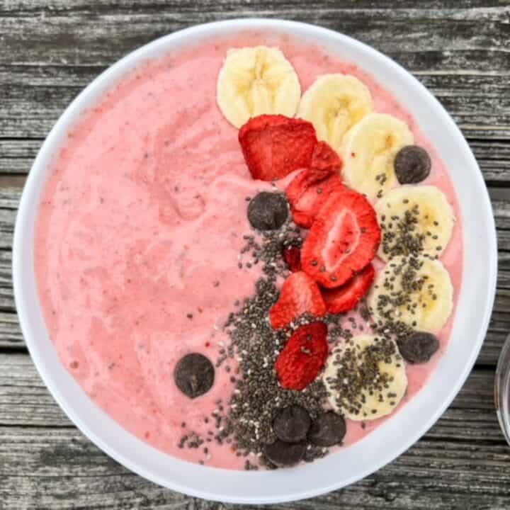 Strawberry banana smoothie bowl served in a white bowl and topped with sliced banana, freeze dried strawberries, chia seeds, and chocolate chips.