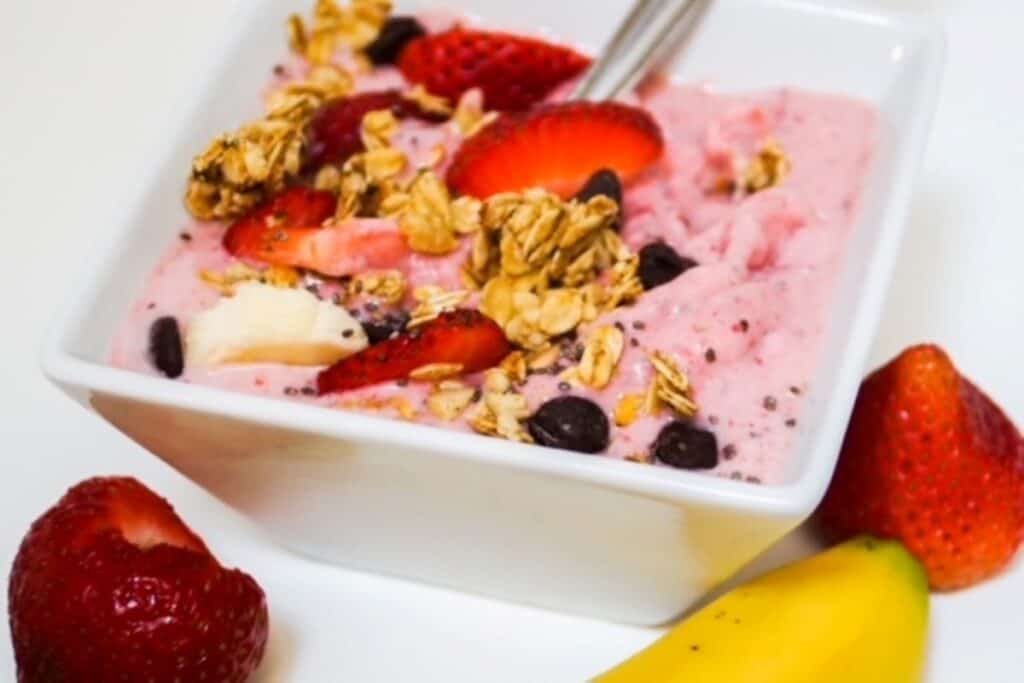 strawberry banana smoothie bowl with toppings in a square white bowl