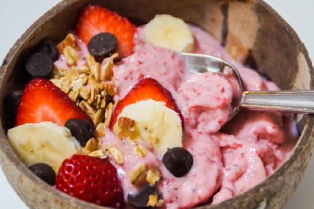 strawberry banana smoothie bowl in a coconut shell bowl with toppings