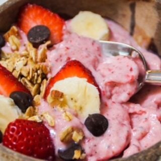strawberry banana smoothie bowl in a coconut shell bowl with toppings