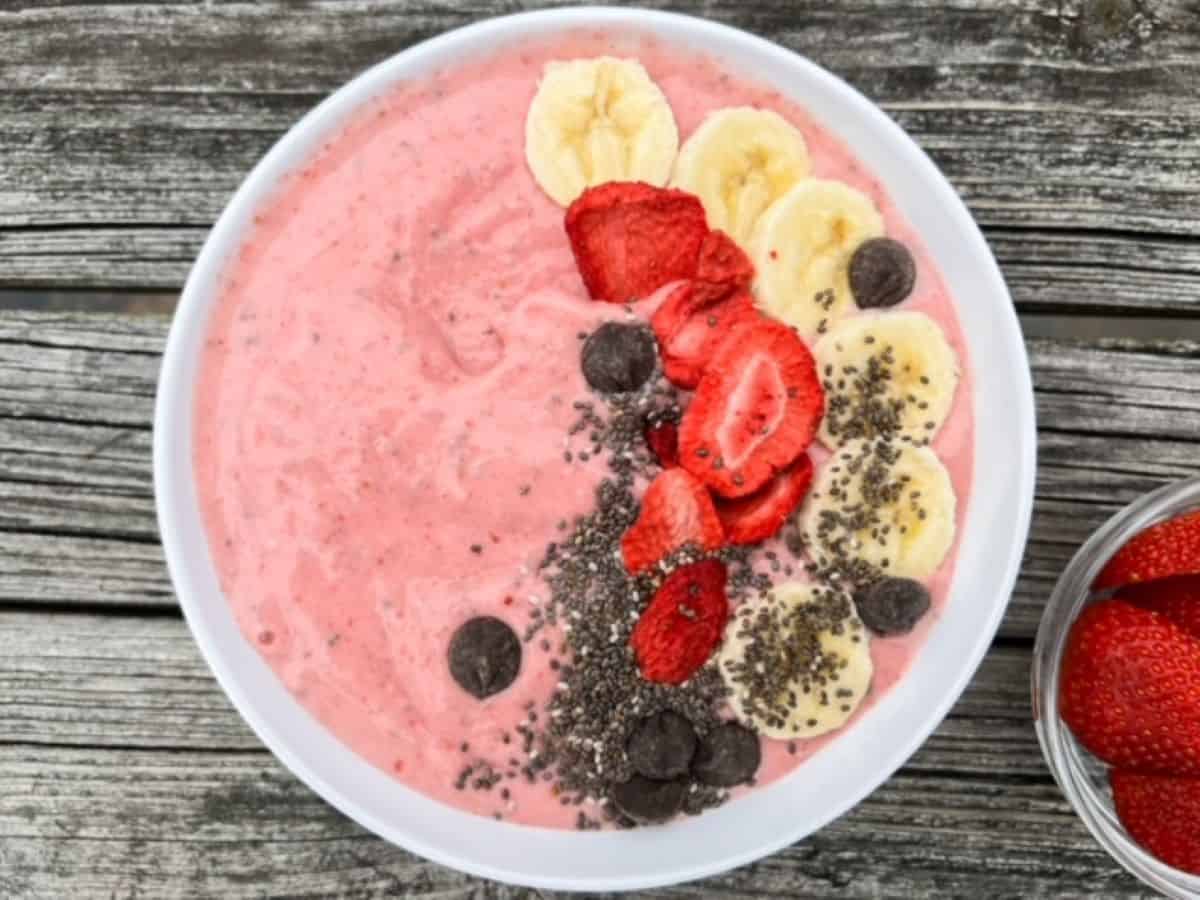 Strawberry banana smoothie bowl topped with banana slices, freeze dried strawberries, chia seeds, and chocolate chips.