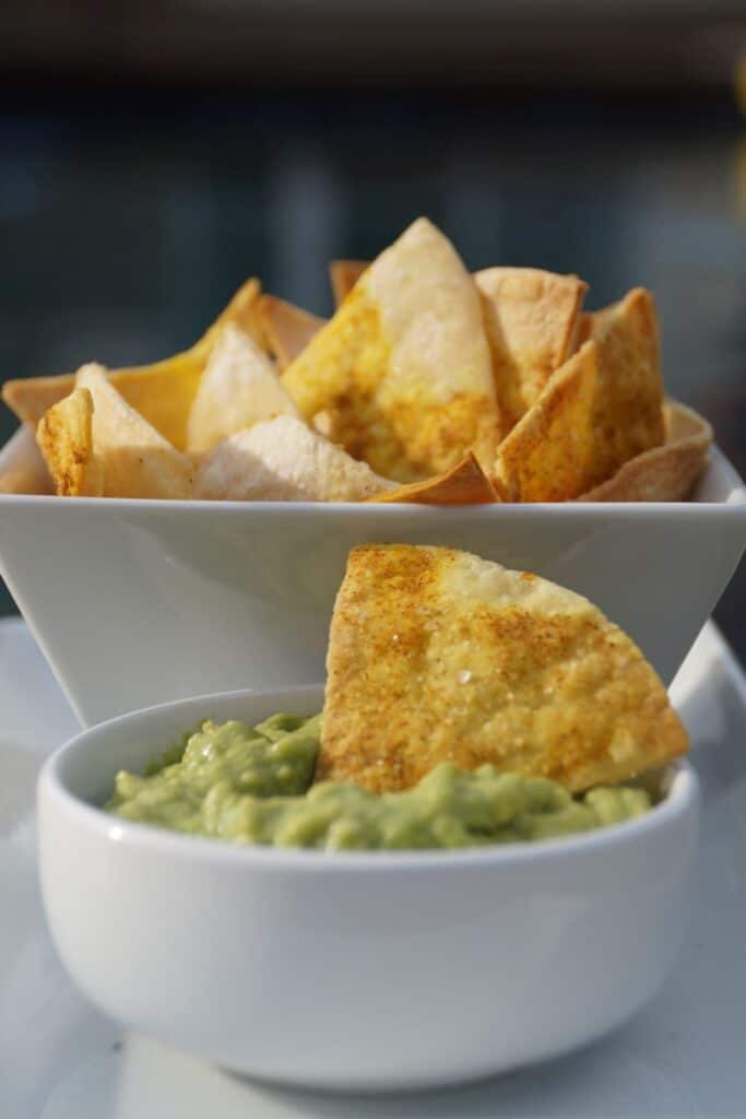 tortilla chip in a bowl of guacamole with a bowl of chips in the background