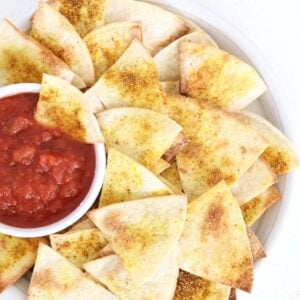 Homemade tortilla chips with salsa on a white plate.