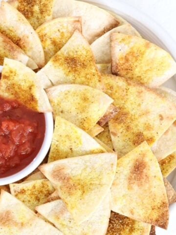 Homemade tortilla chips with salsa on a white plate.