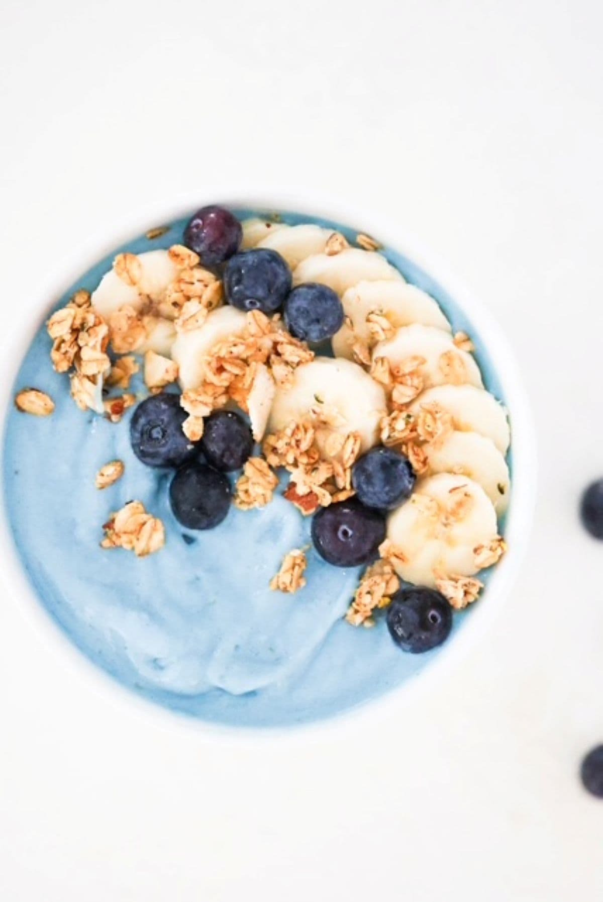 Blue smoothie bowl topped with banana slices, blueberries, and granola.