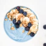 Blue smoothie bowl topped with sliced banana, blueberries, and granola.