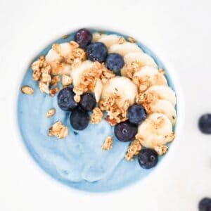 Blue smoothie bowl topped with sliced banana, blueberries, and granola.