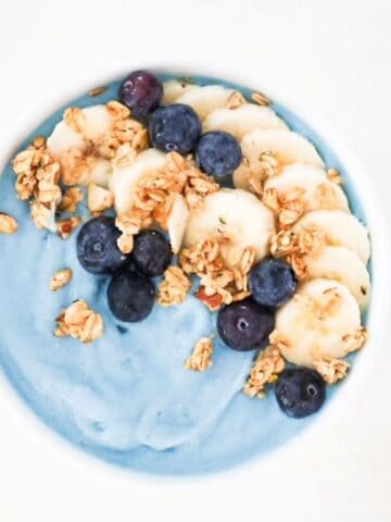Blue smoothie bowl topped with sliced banana, blueberries, and granola.