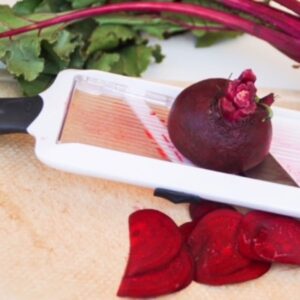 Beet being sliced with a mandolin slicer over a cutting board.