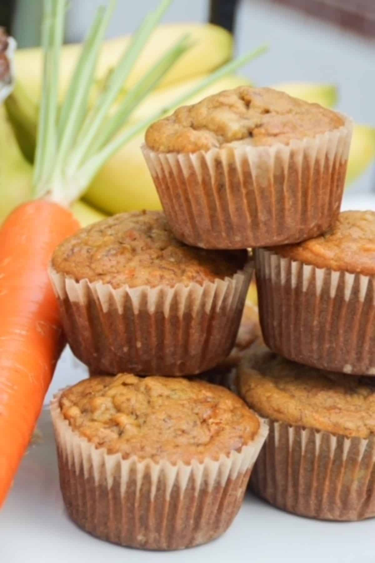 Stacked muffins with a carrot and bananas in the background