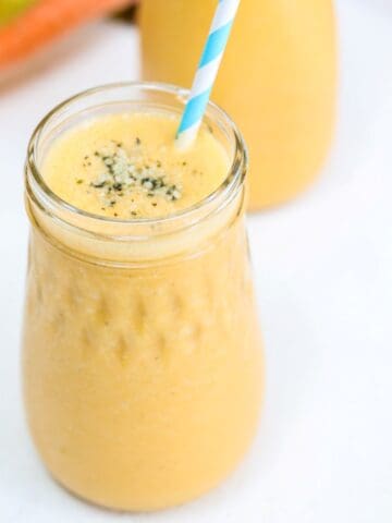 One Carrot Banana Smoothie in a glass jar with a blue and white striped straw.