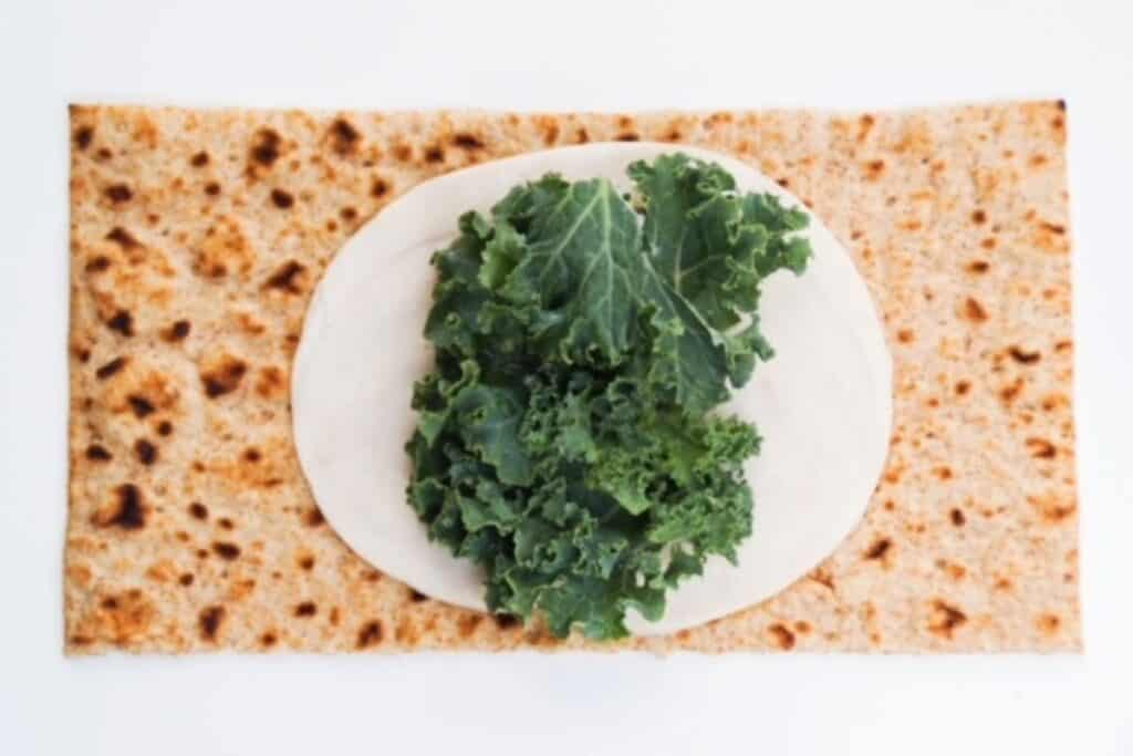 open flatbread topped with one slice of chicken and a small handful of kale