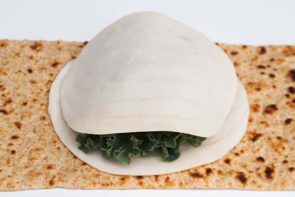 flatbread laid out topped with once slice of turkey, kale, and a second slice of turkey