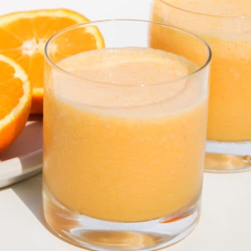 two glasses of orange carrot smoothie with a freshly sliced orange