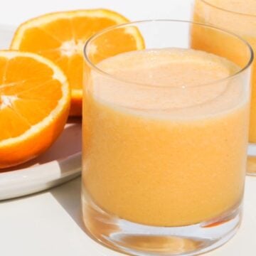 two glasses of orange carrot smoothie with two halves of a fresh orange