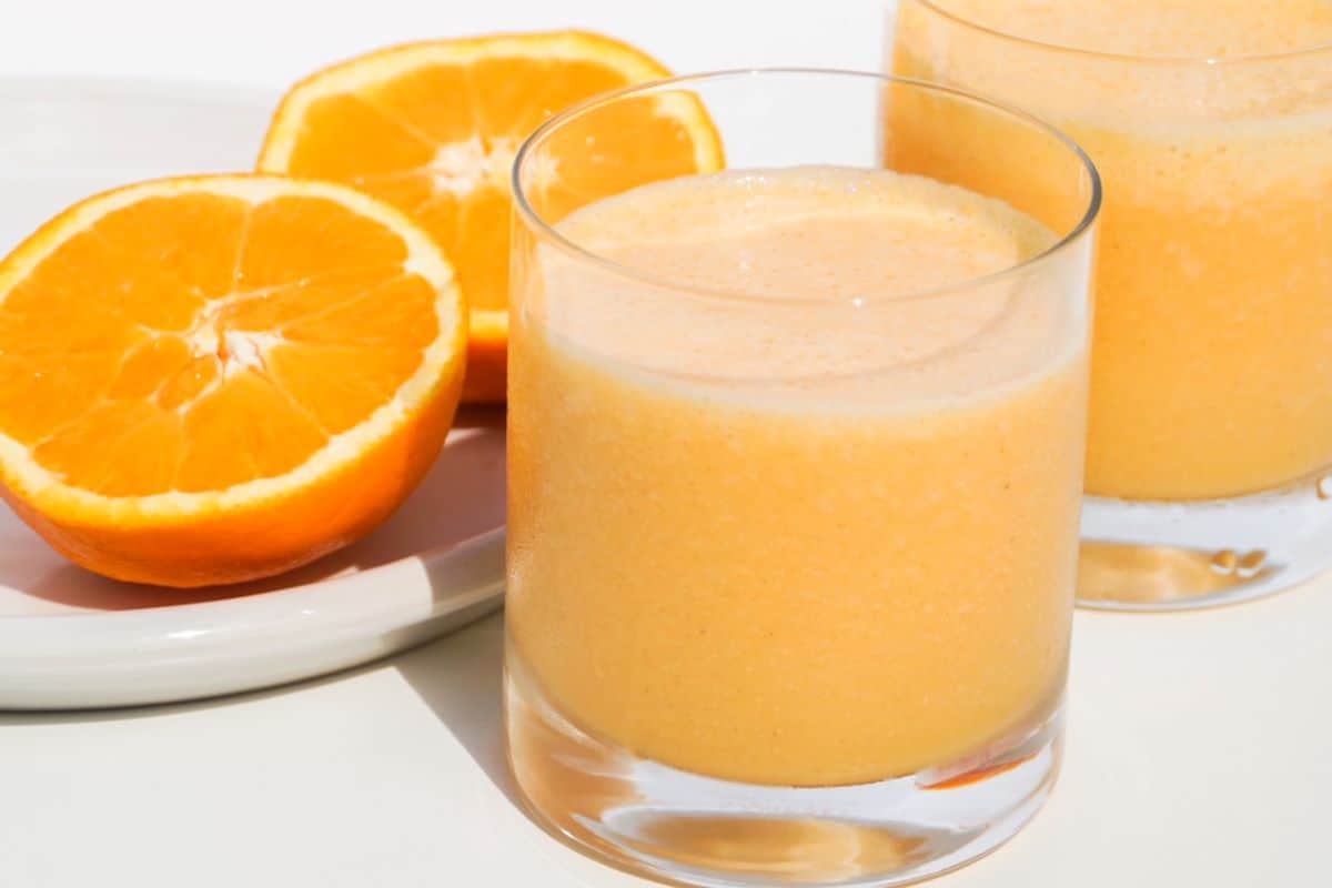 Two glasses of carrot smoothie with two halves of a fresh orange