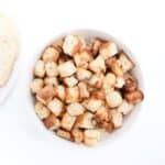 Air fryer croutons in a white bowl with a loaf of bread seen to the left.