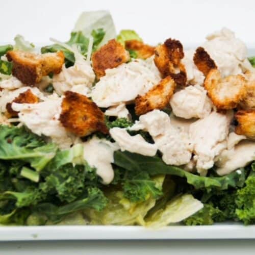 Chicken Caesar Salad ingredients layered on a white plate.