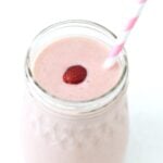 Strawberry banana smoothie in a glass jar, topped with a strawberry and served with a pink and white straw.