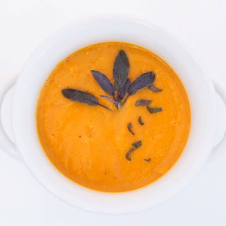 Butternut squash soup topped with fresh sage, in a white bowl.