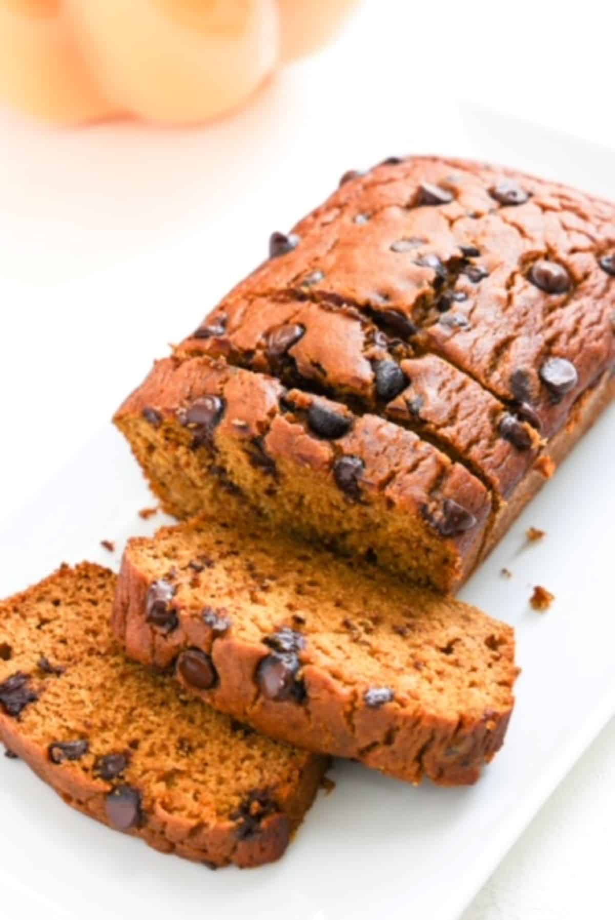 One loaf of pumpkin bread topped with chocolate chips and sliced. Part of a decorative pumpkin is in the background.