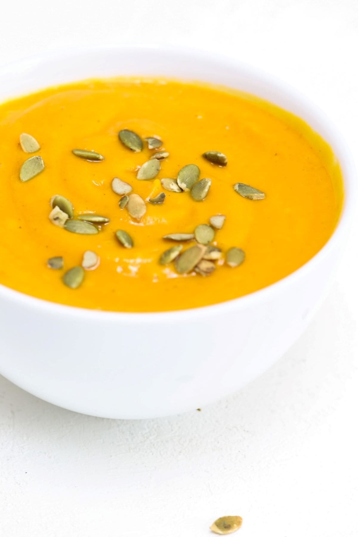 Carrot Butternut Squash Soup in a white bowl and topped with pumpkin seeds.