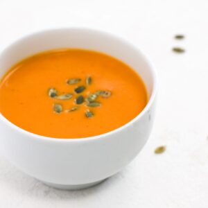 Butternut squash soup topped with pumpkin seeds in a white bowl.