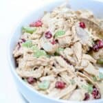 Up close picture of chicken pomegranate salad in a white bowl with a gold serving spoon.