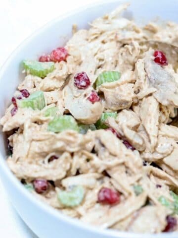 Up close picture of chicken pomegranate salad in a white bowl with a gold serving spoon.