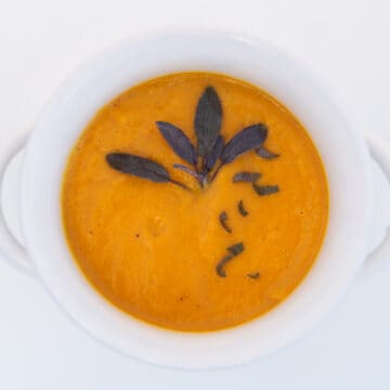 Butternut squash soup in a white bowl, topped with fresh sage leaves.