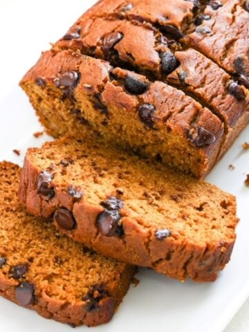 Half of a loaf of pumpkin chocolate chop bread sliced on white plate.