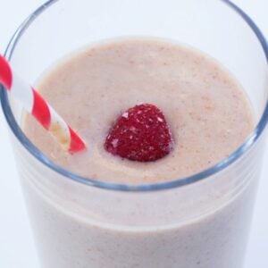 Smoothie in a glass with one frozen strawberry and a straw.