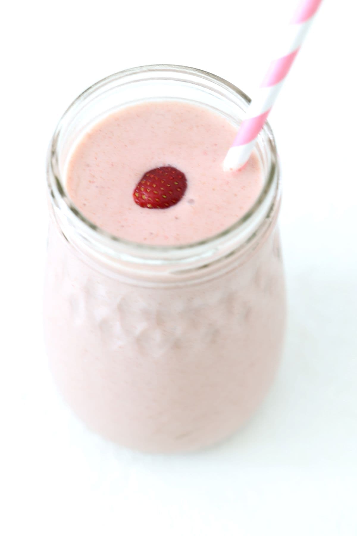 One strawberry peanut butter banana smoothie in a glass jar with a pink and white striped straw.