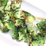Roasted broccoli on a white rectangular shaped plate with a gold spoon.