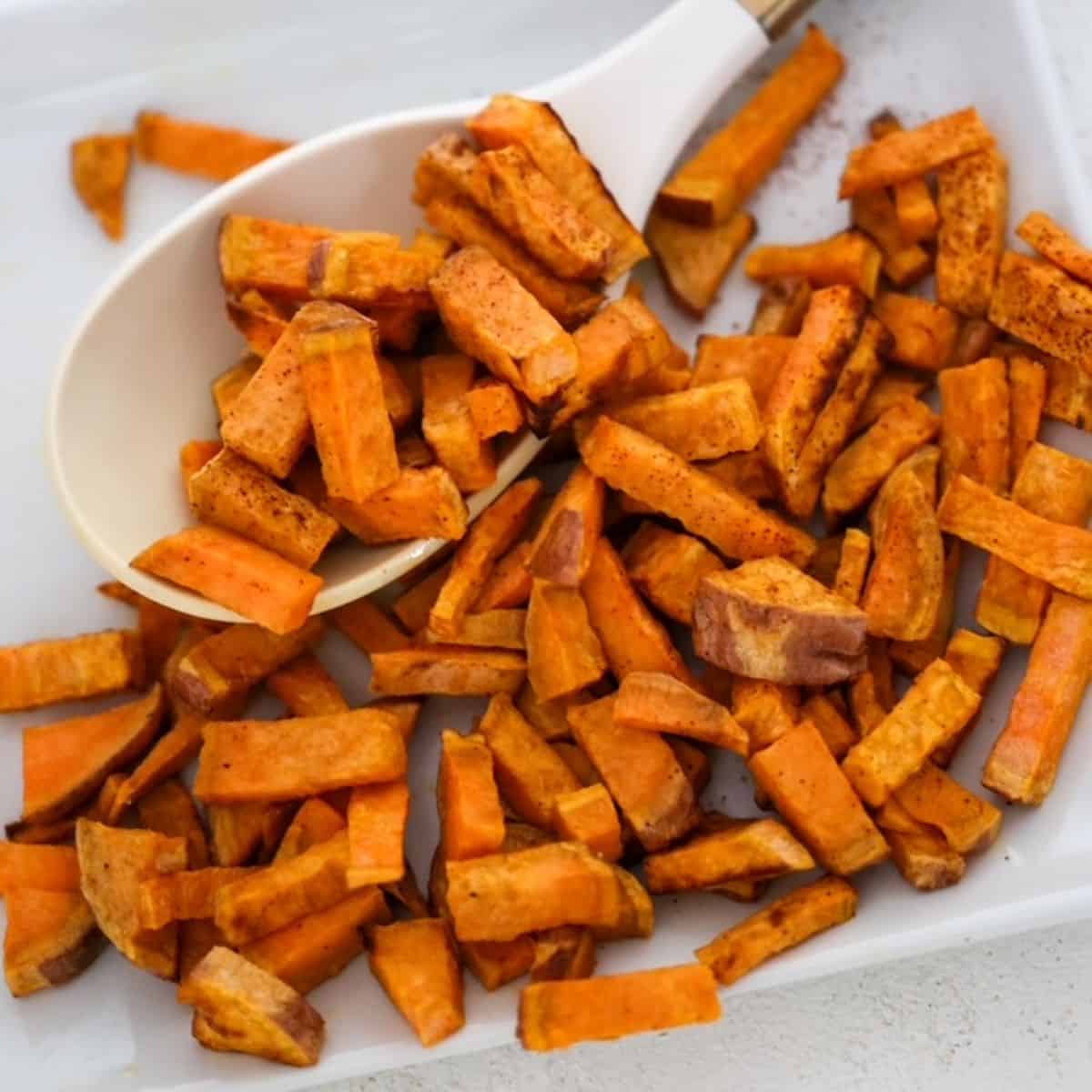 Chunks of roasted sweet potatoes on a white plate with a white and gold serving spoon.